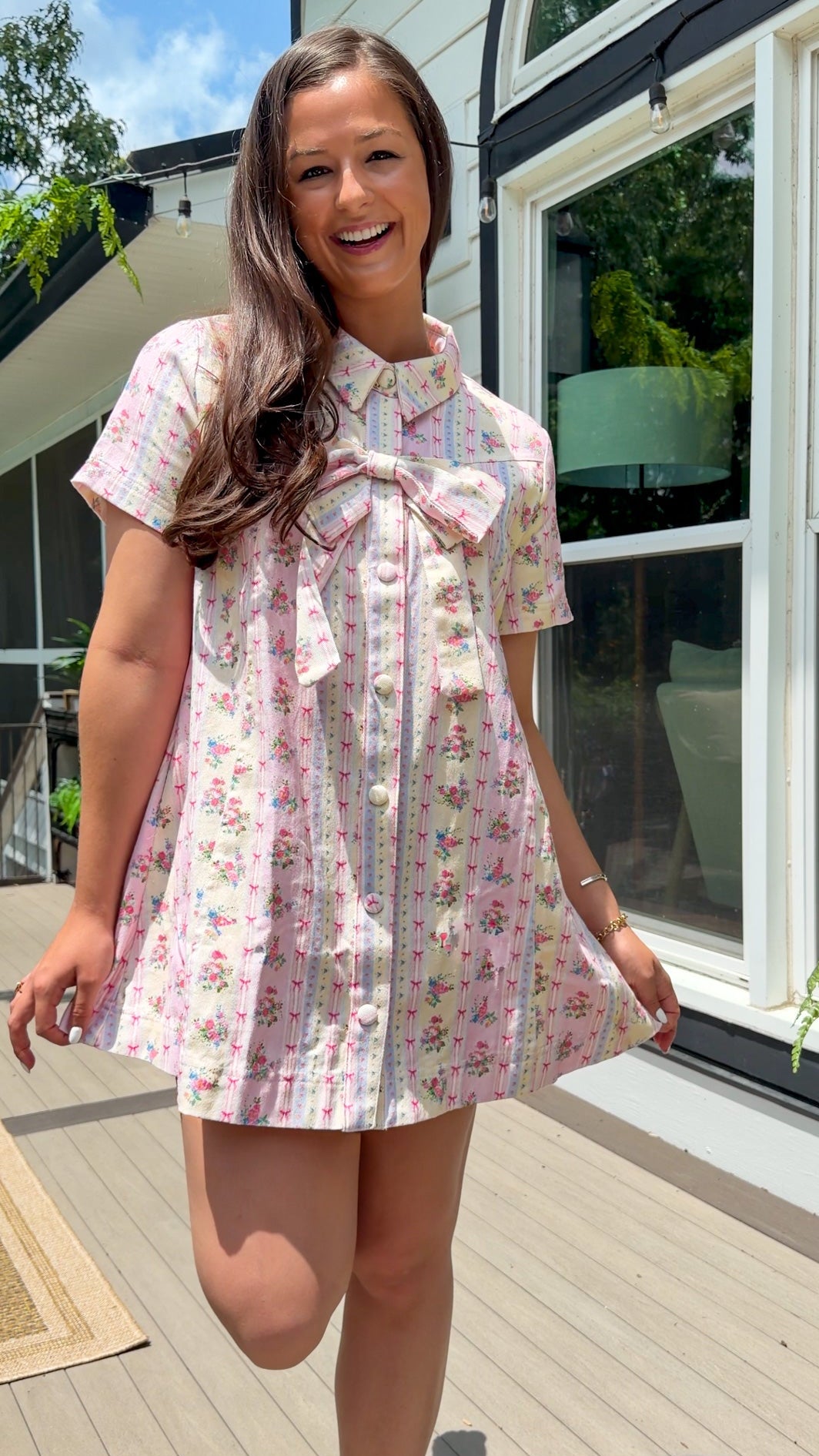 Light pink floral stripe mini dress with a collared neckline, front button closure, short sleeves, oversized bow detail, and relaxed A-line silhouette.