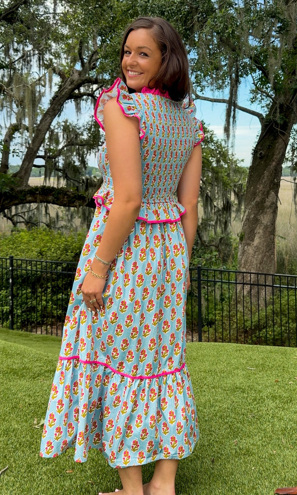 Light blue floral print midi dress featuring a fully smocked bodice, flutter sleeves with pink contrast trim, a keyhole tie neckline, ruffled peplum waist, tiered midi skirt, and side pockets.