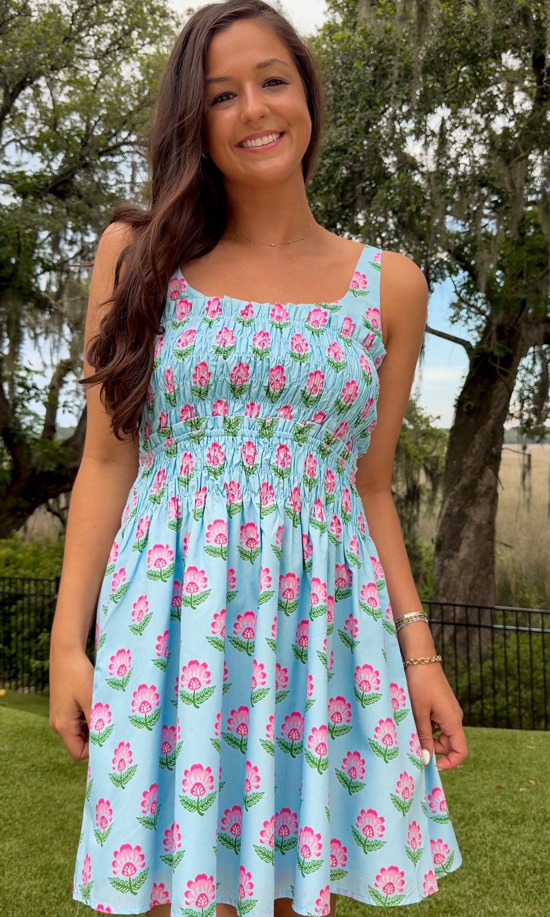 Light blue floral print mini dress featuring a softly scooped neckline, wide shoulder straps, a fully smocked bodice, side pockets, and a flowy flared skirt.