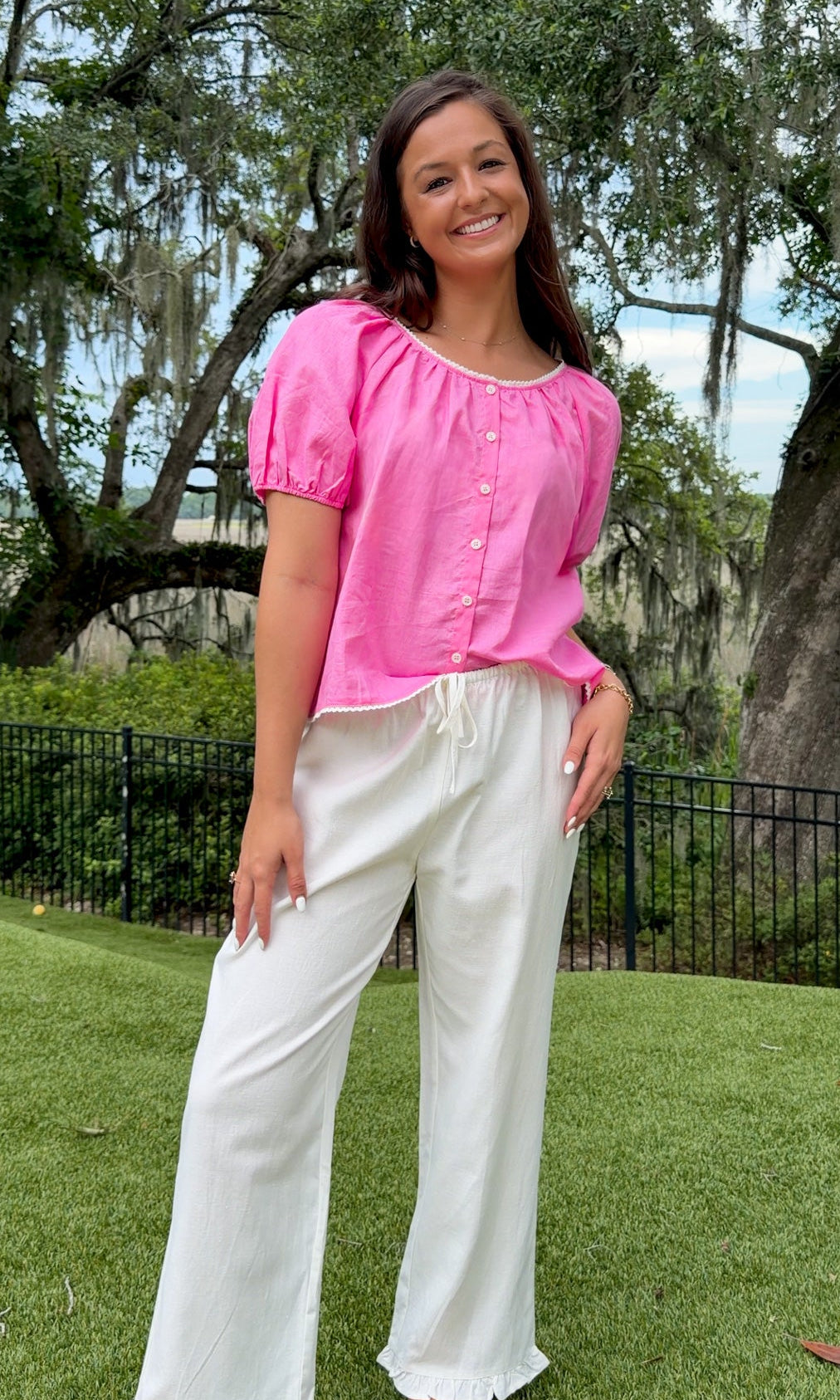 Pink lightweight woven top featuring a gathered scoop neckline with delicate white lace trim, functional front buttons, short puff sleeves, and a relaxed silhouette.