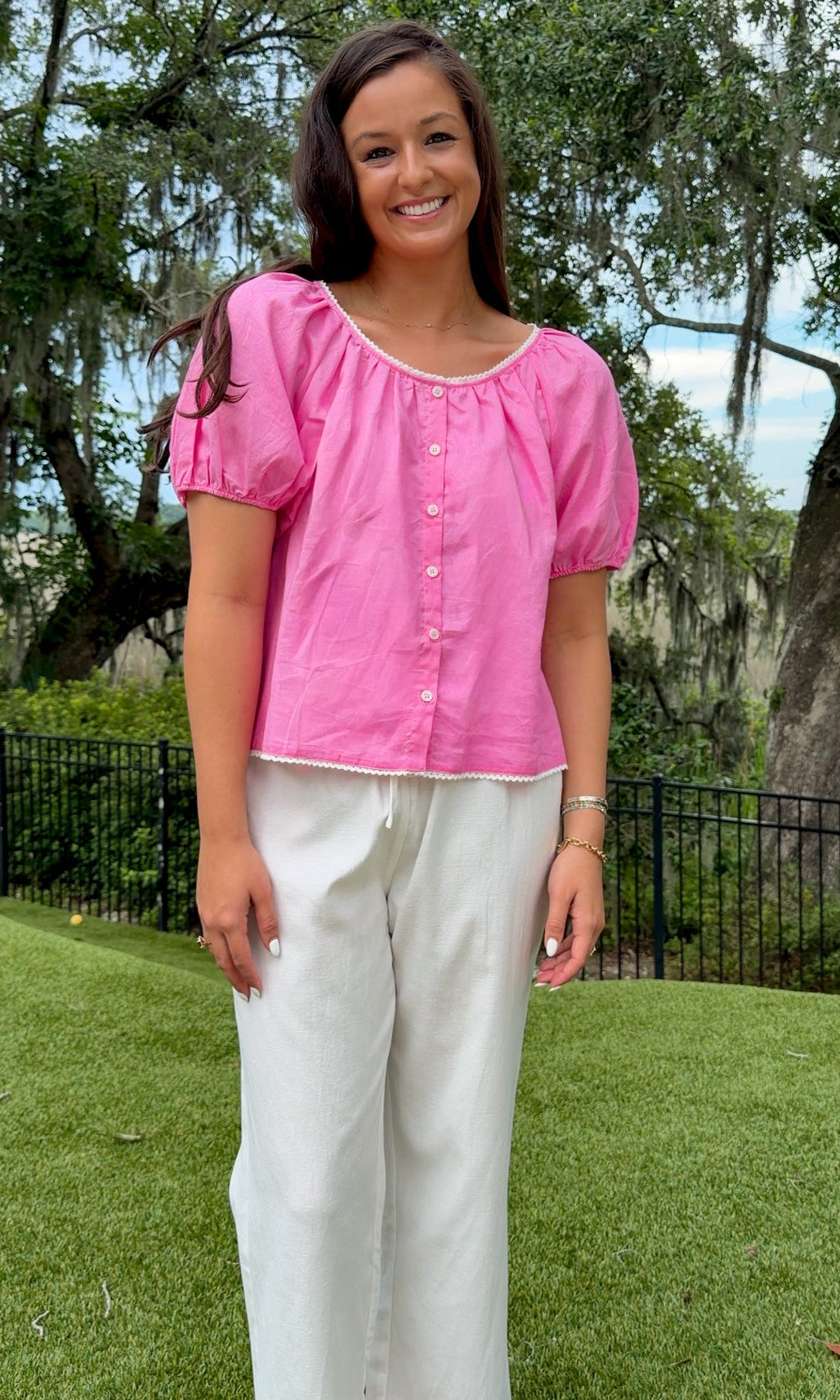 Pink lightweight woven top featuring a gathered scoop neckline with delicate white lace trim, functional front buttons, short puff sleeves, and a relaxed silhouette.