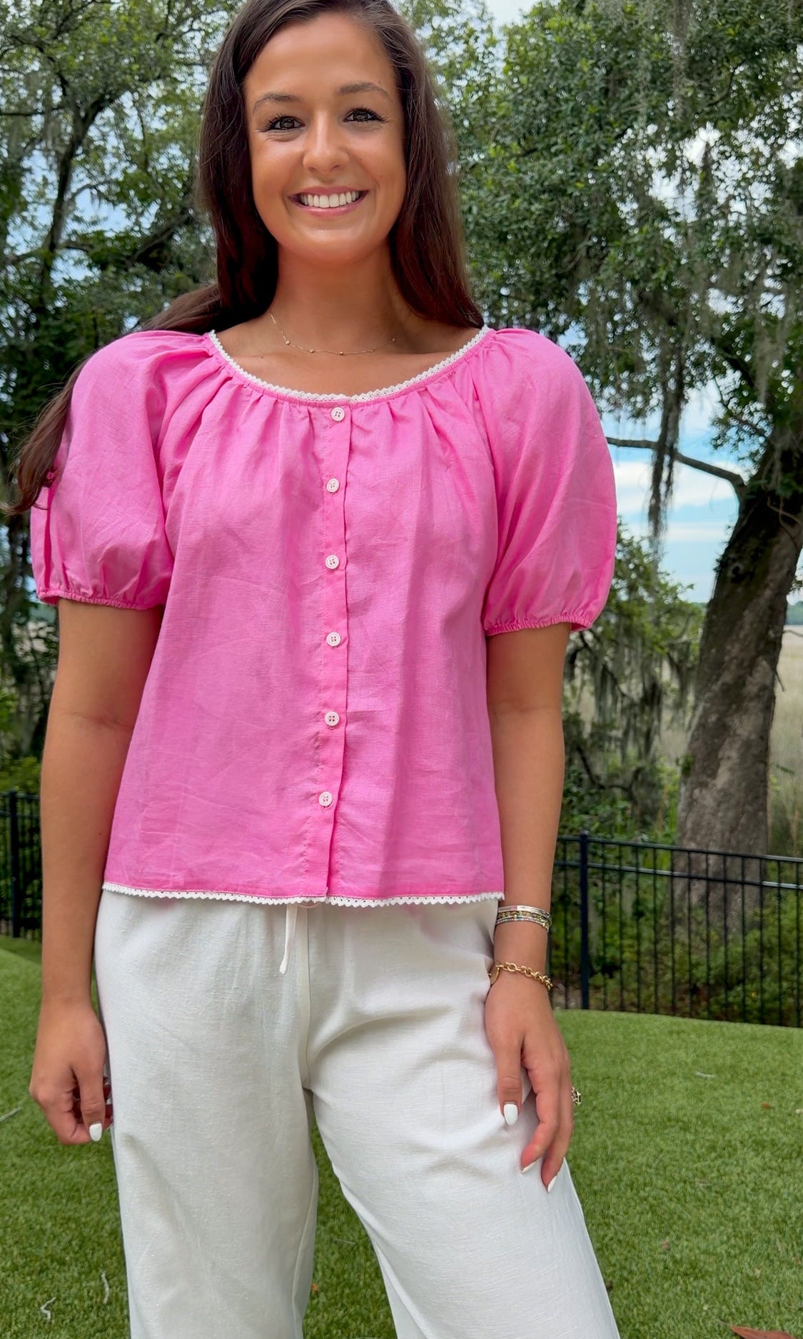 Pink lightweight woven top featuring a gathered scoop neckline with delicate white lace trim, functional front buttons, short puff sleeves, and a relaxed silhouette.
