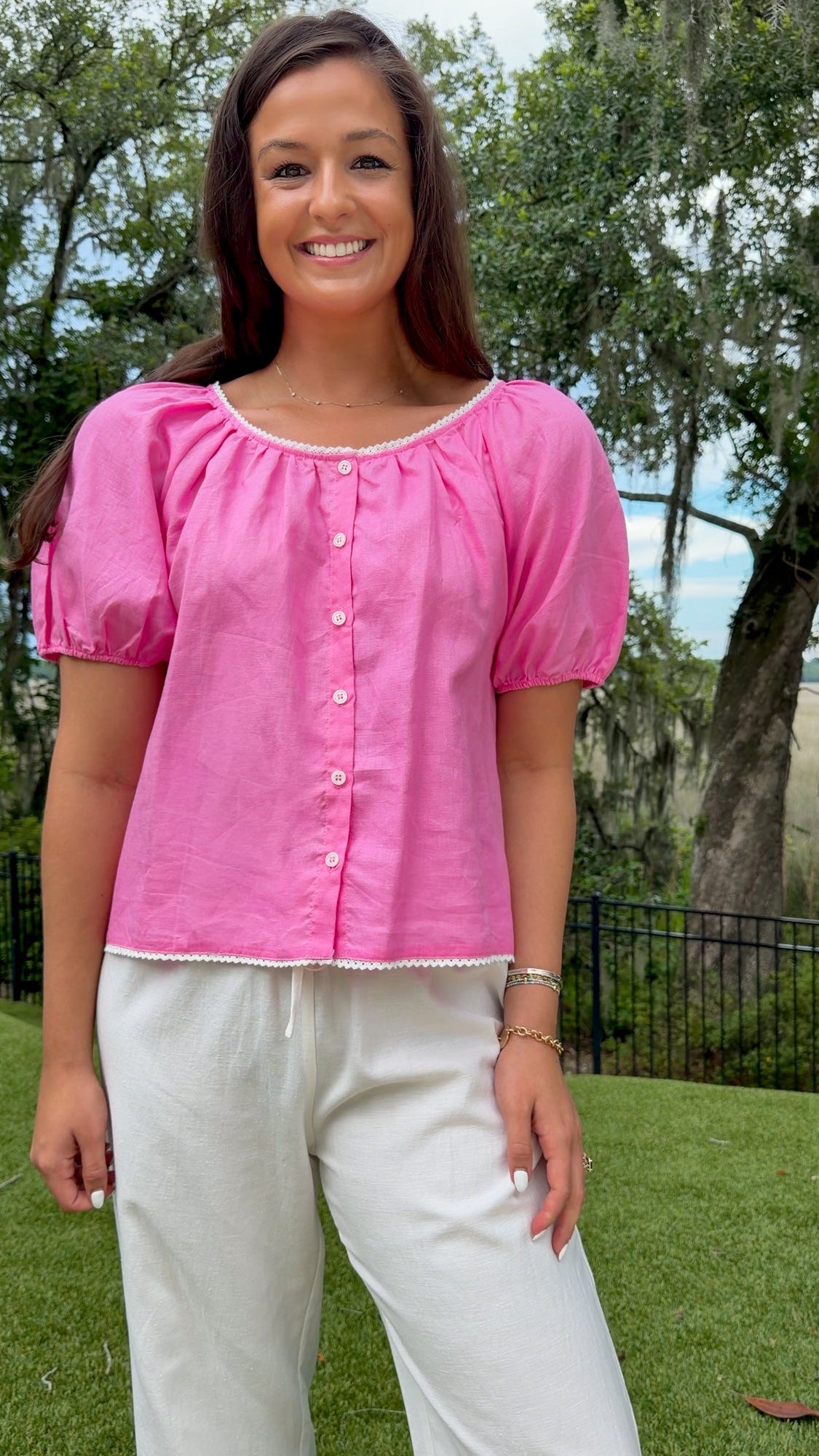 Pink lightweight woven top featuring a gathered scoop neckline with delicate white lace trim, functional front buttons, short puff sleeves, and a relaxed silhouette.