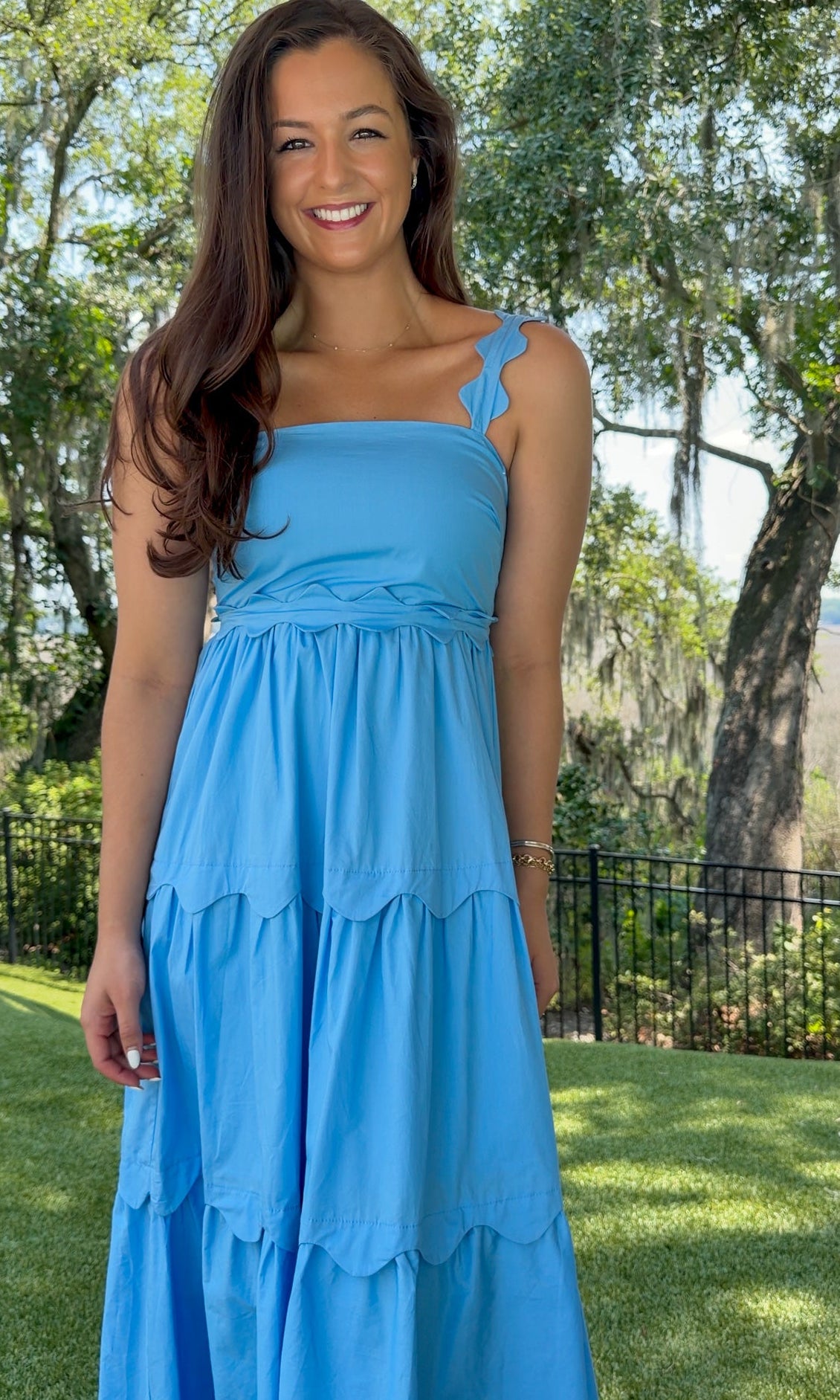 Blue midi dress featuring a square neckline, adjustable scalloped shoulder straps, scalloped trim at the empire waist and tiered skirt, a smocked back, and a flowing A-line silhouette.