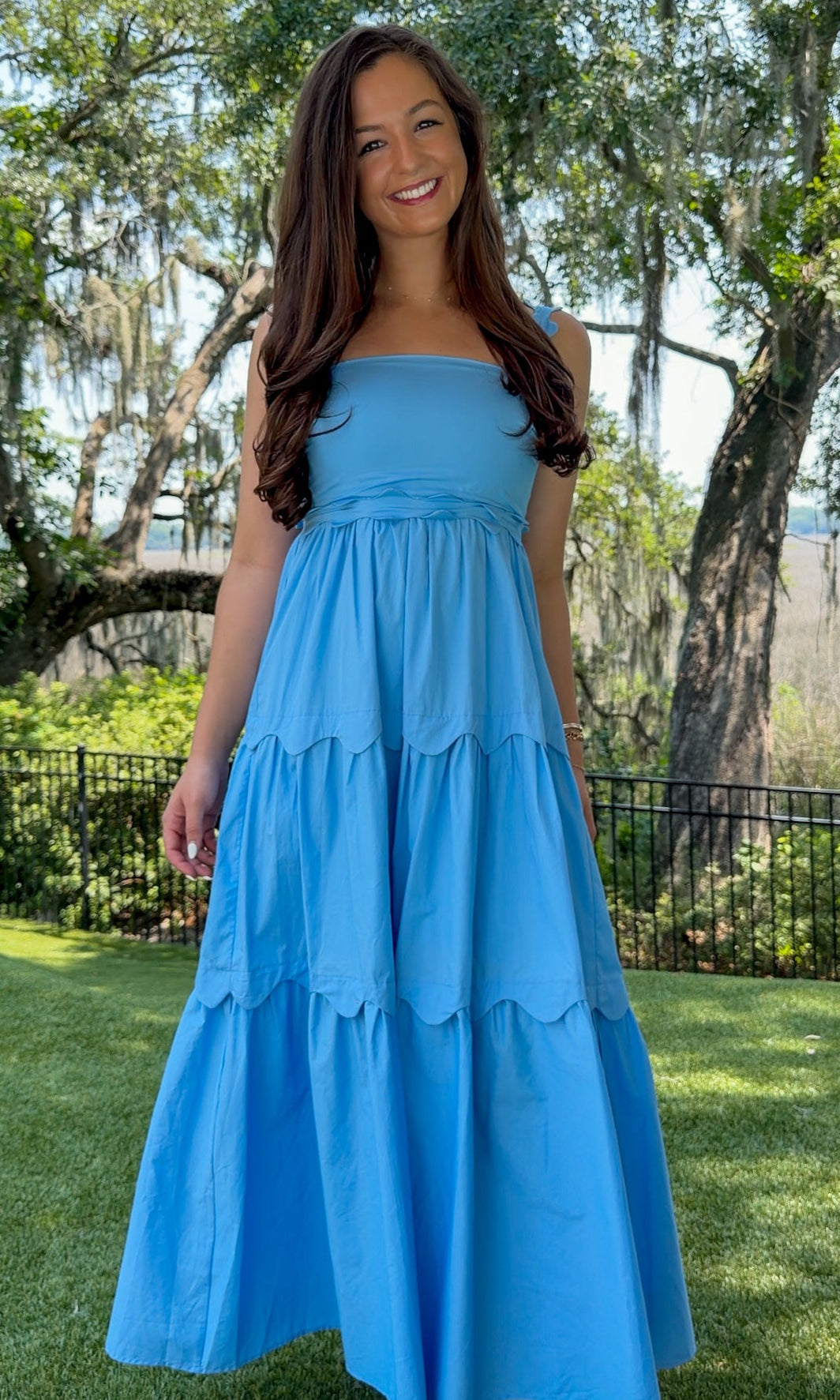 Blue midi dress featuring a square neckline, adjustable scalloped shoulder straps, scalloped trim at the empire waist and tiered skirt, a smocked back, and a flowing A-line silhouette.