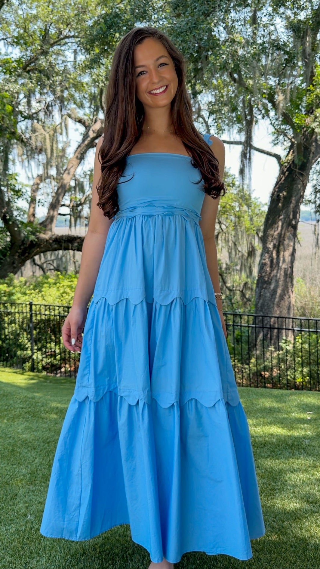 Blue midi dress featuring a square neckline, adjustable scalloped shoulder straps, scalloped trim at the empire waist and tiered skirt, a smocked back, and a flowing A-line silhouette.