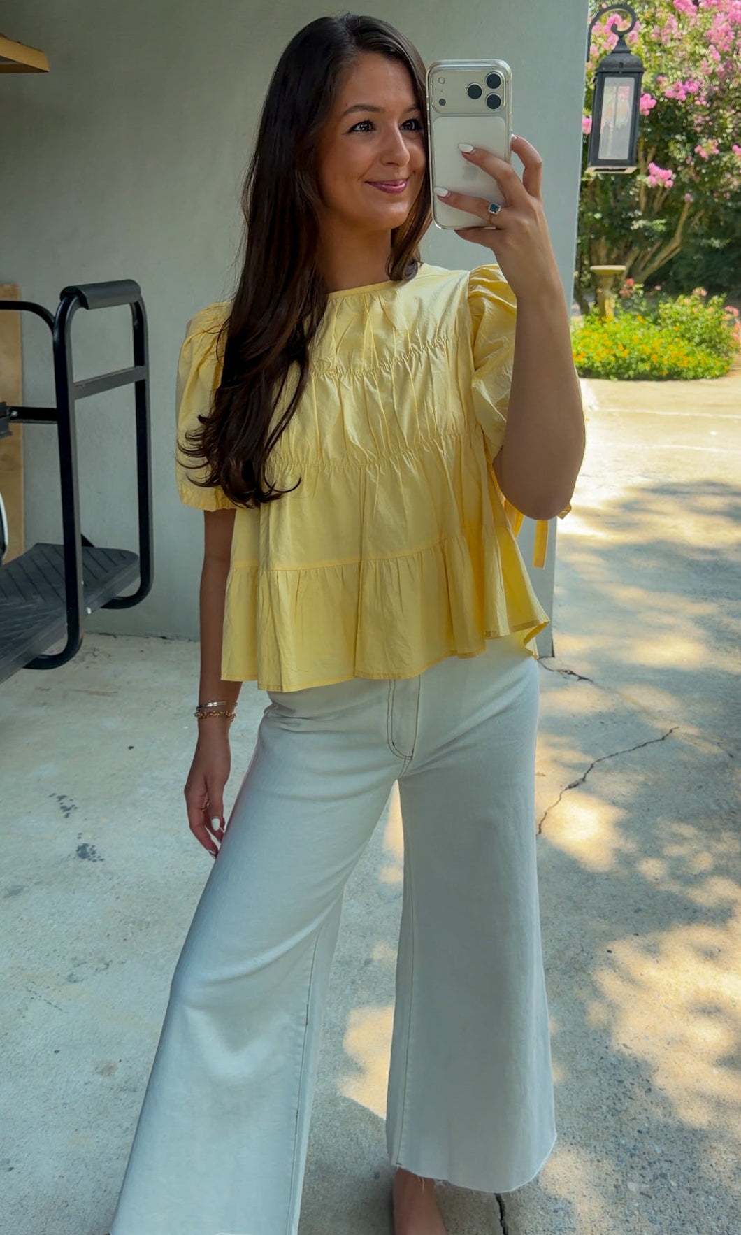 Butter yellow babydoll top featuring a round neckline, tiered shirring, short puff sleeves with adjustable tie cuffs, a ruffle-trimmed back, keyhole button closure, and a relaxed semi-cropped silhouette.