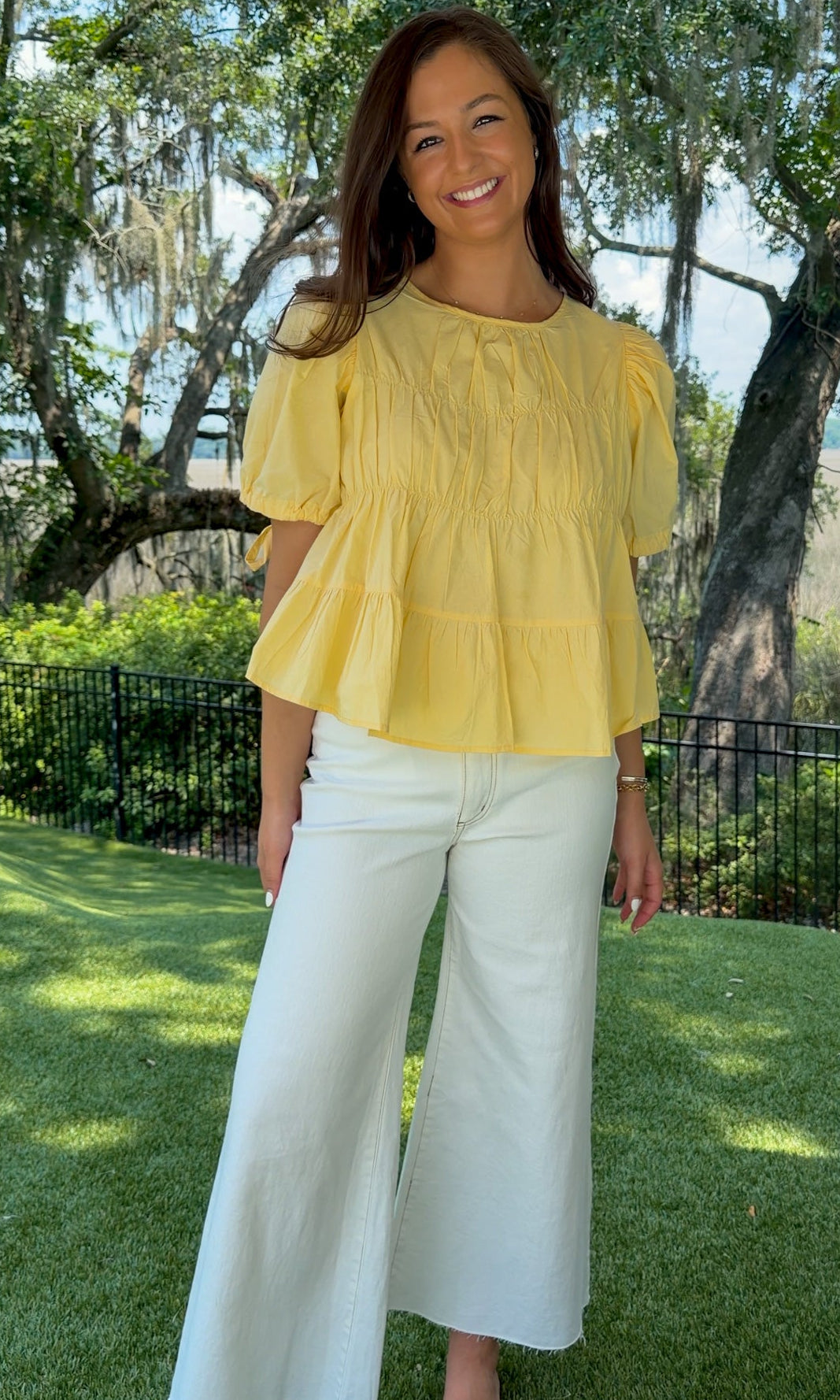 Butter yellow babydoll top featuring a round neckline, tiered shirring, short puff sleeves with adjustable tie cuffs, a ruffle-trimmed back, keyhole button closure, and a relaxed semi-cropped silhouette.