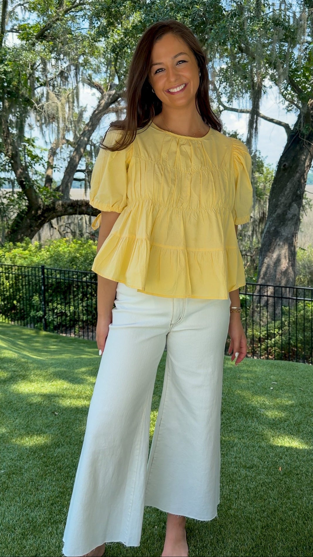 Butter yellow babydoll top featuring a round neckline, tiered shirring, short puff sleeves with adjustable tie cuffs, a ruffle-trimmed back, keyhole button closure, and a relaxed semi-cropped silhouette.