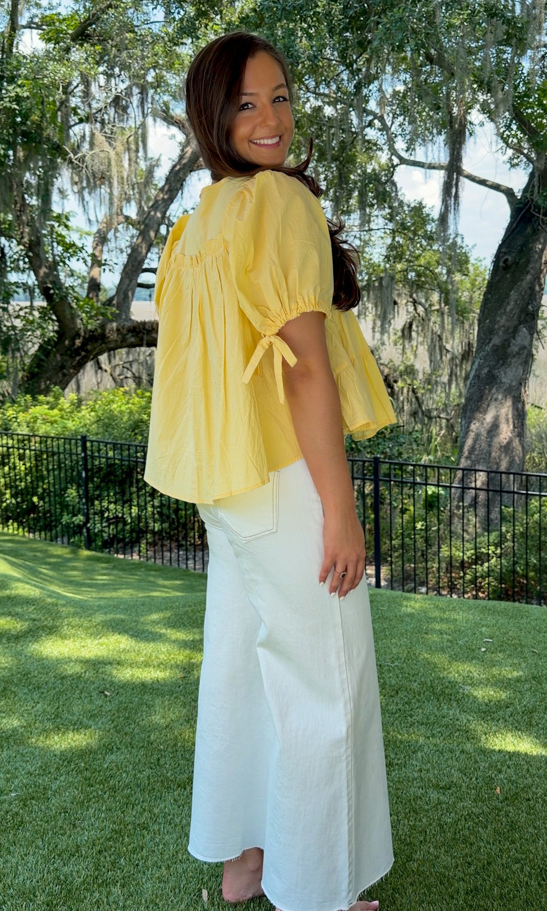 Butter yellow babydoll top featuring a round neckline, tiered shirring, short puff sleeves with adjustable tie cuffs, a ruffle-trimmed back, keyhole button closure, and a relaxed semi-cropped silhouette.