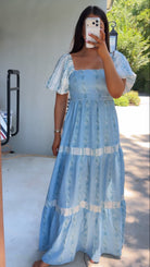 Woman wearing a blue lace dress taking a mirror selfie outdoors.