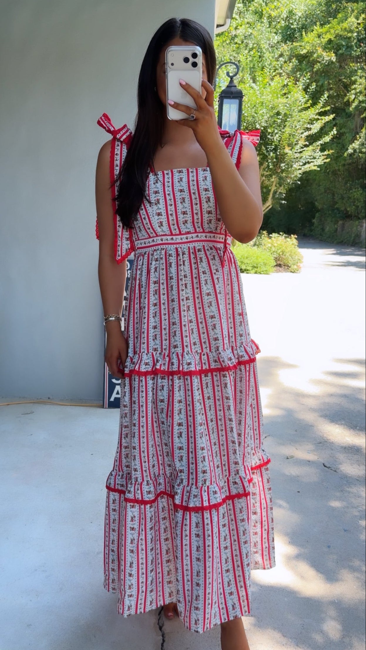 Woman wearing a red and white patterned dress taking a mirror selfie outdoors.