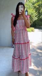 Woman wearing a red and white patterned dress taking a mirror selfie outdoors.