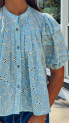 Woman wearing a yellow blouse with a pattern and blue jeans standing on a wooden deck.