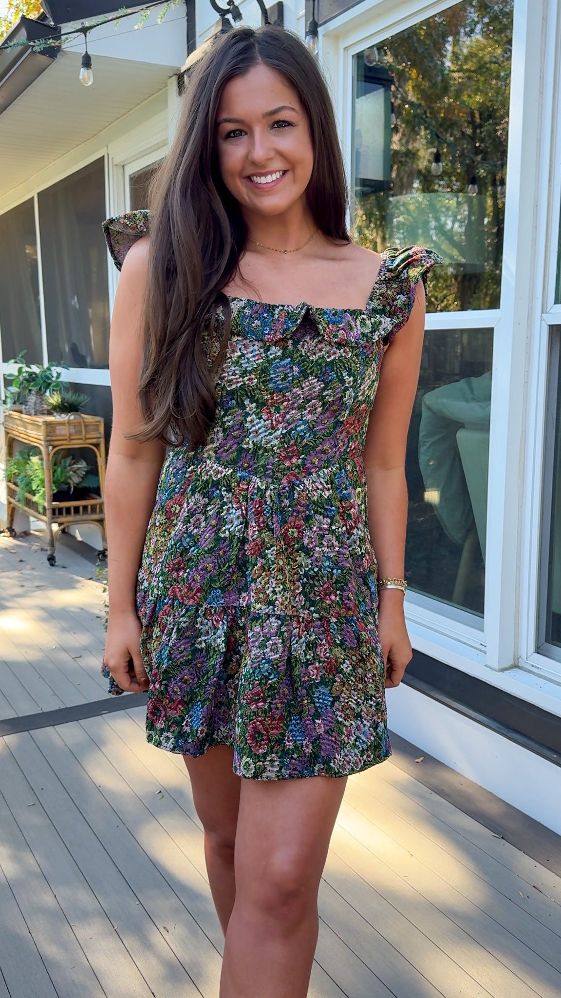 Woman wearing a floral dress standing on a wooden deck.