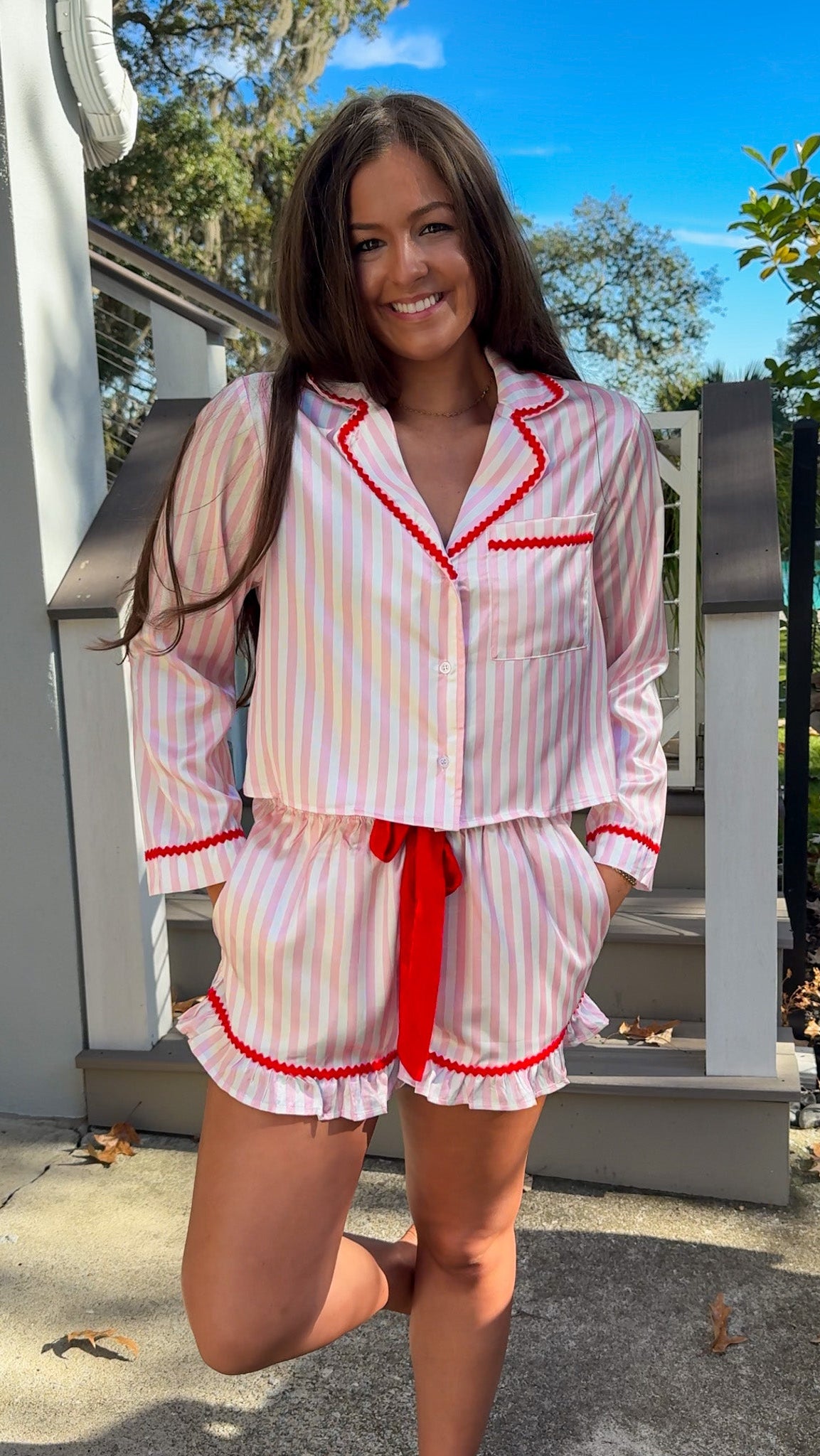 Woman wearing a pink and white striped pajama set with red accents outdoors. christmas pajamas