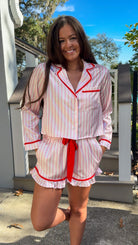 Woman wearing a pink and white striped pajama set with red accents outdoors. christmas pajamas