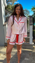 Woman wearing a pink and white striped pajama set with red accents outdoors. christmas pajamas merry and bright wording on back close