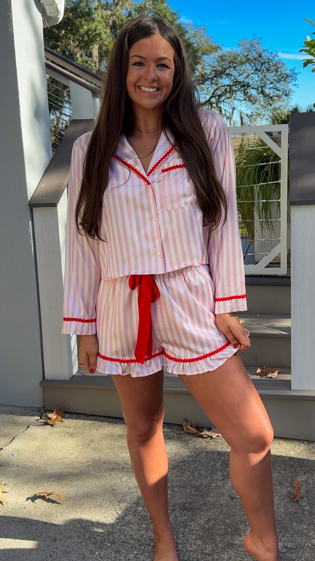 Woman wearing a pink and white striped pajama set with red accents outdoors. christmas pajamas merry and bright wording on back cute