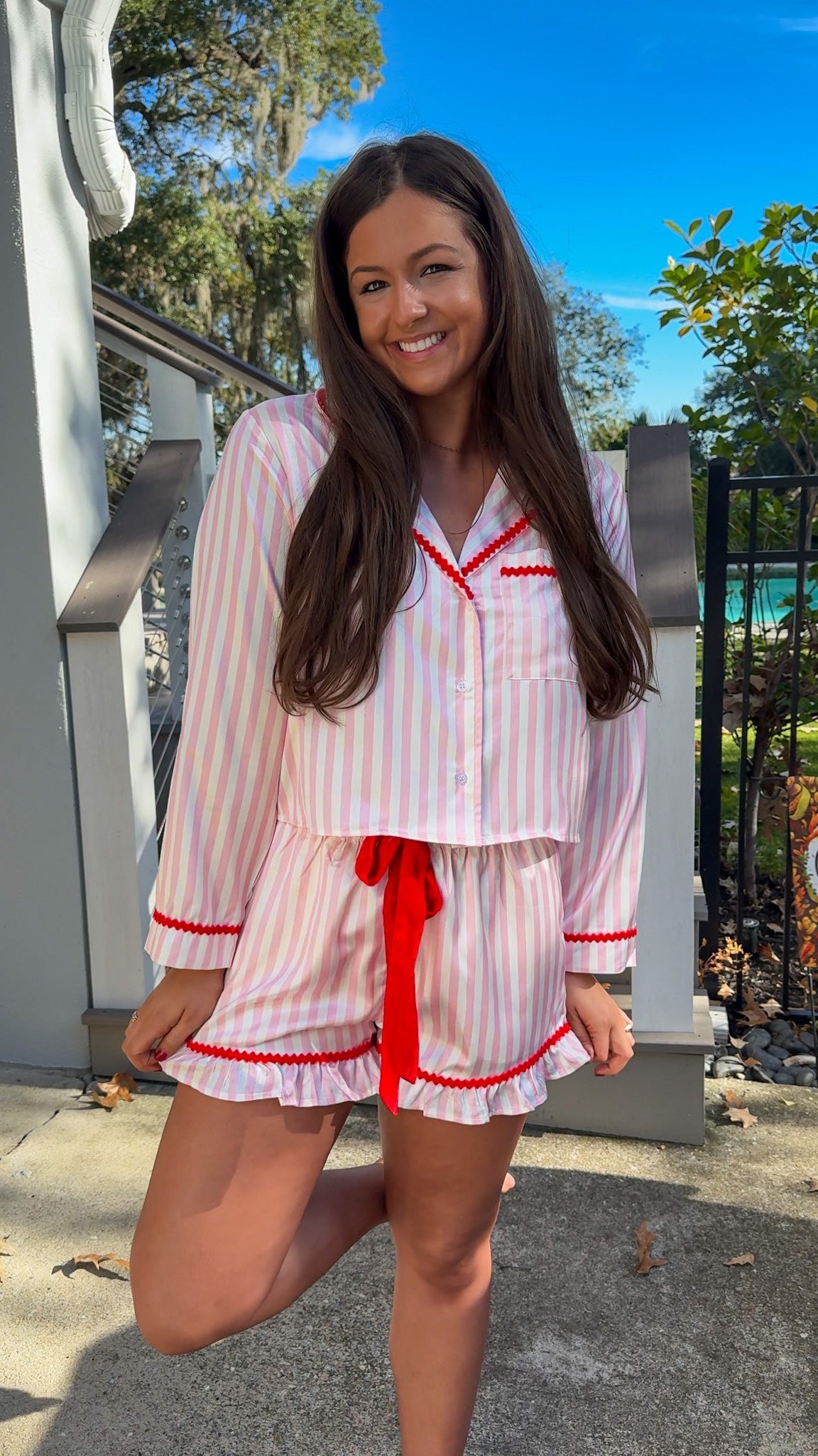 Woman wearing a pink and white striped pajama set with red accents outdoors. christmas pajamas merry and bright wording on back 1