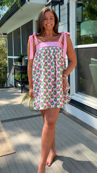 Woman in a floral dress standing on a wooden deck with a house in the background