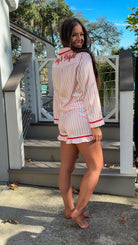 Woman wearing a pink and white striped pajama set with red accents outdoors. christmas pajamas merry and bright wording on back