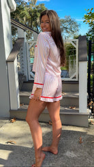 Woman wearing a pink and white striped pajama set with red accents outdoors. christmas pajamas merry and bright wording on back side