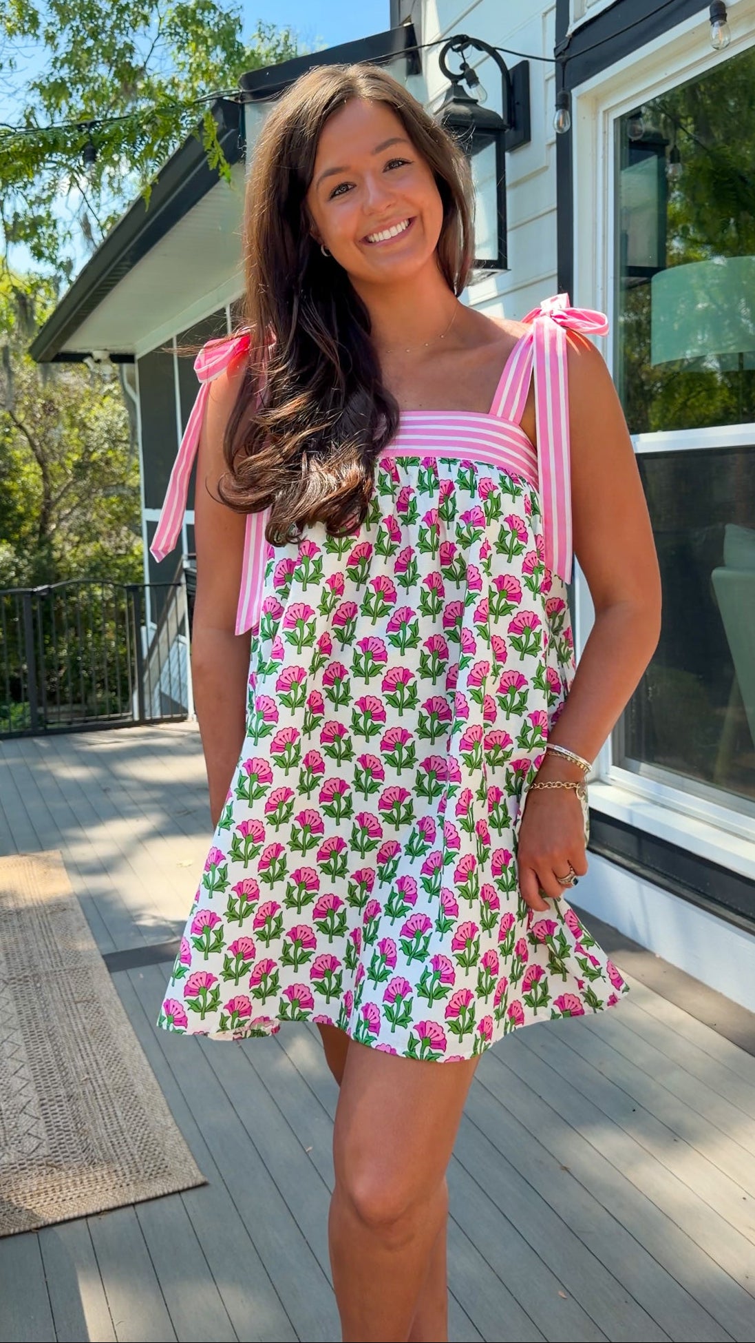 Woman wearing a pink floral dress standing on a wooden deck.