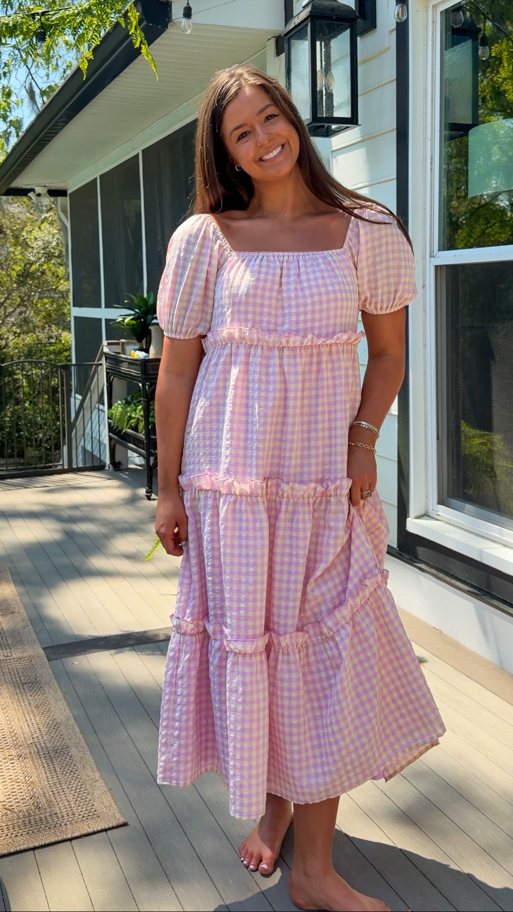 Woman in a pink checkered dress standing outside a house.