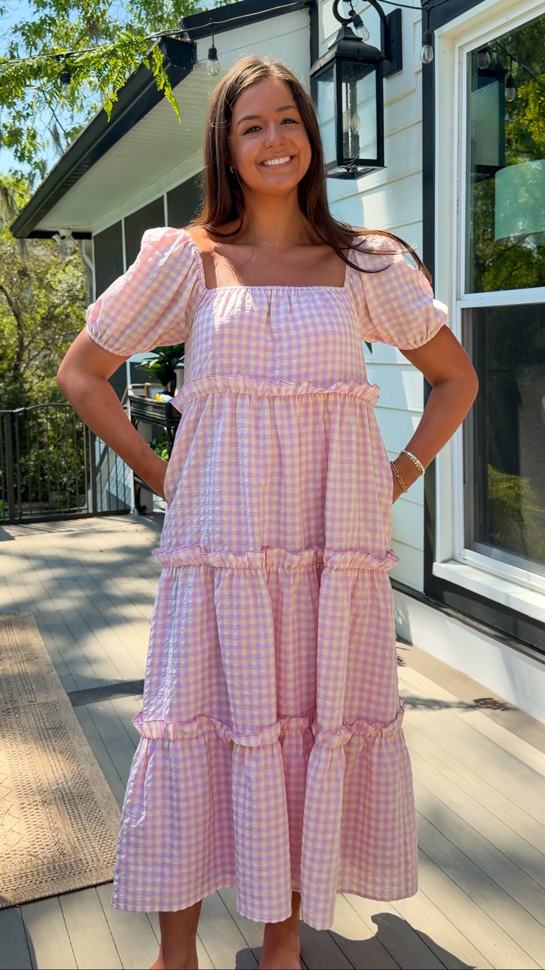 Woman wearing a pink checkered dress standing outside a house.