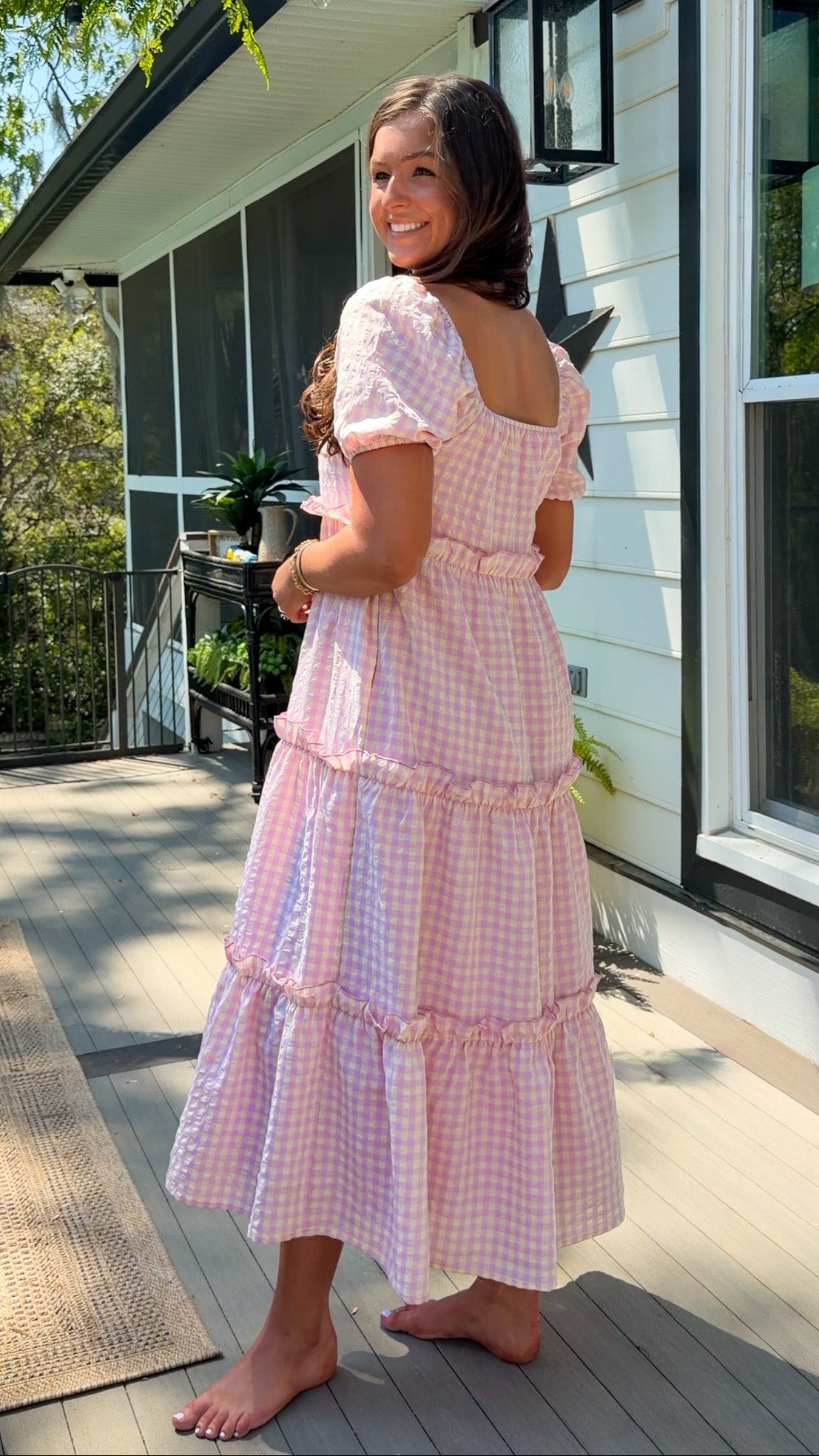 Woman in a pink checkered dress standing on a porch.