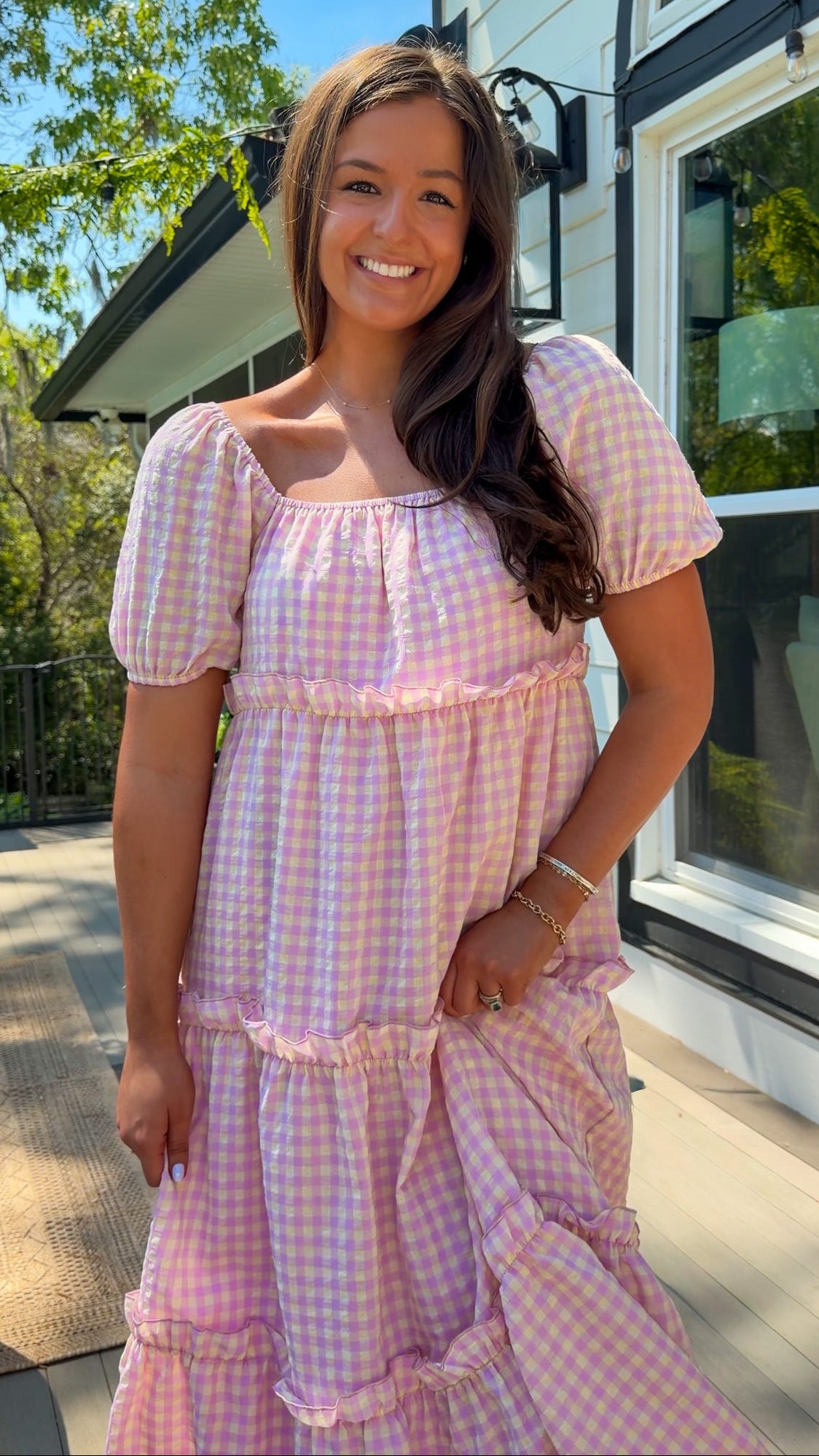 Woman wearing a pink checkered dress standing outdoors near a building.