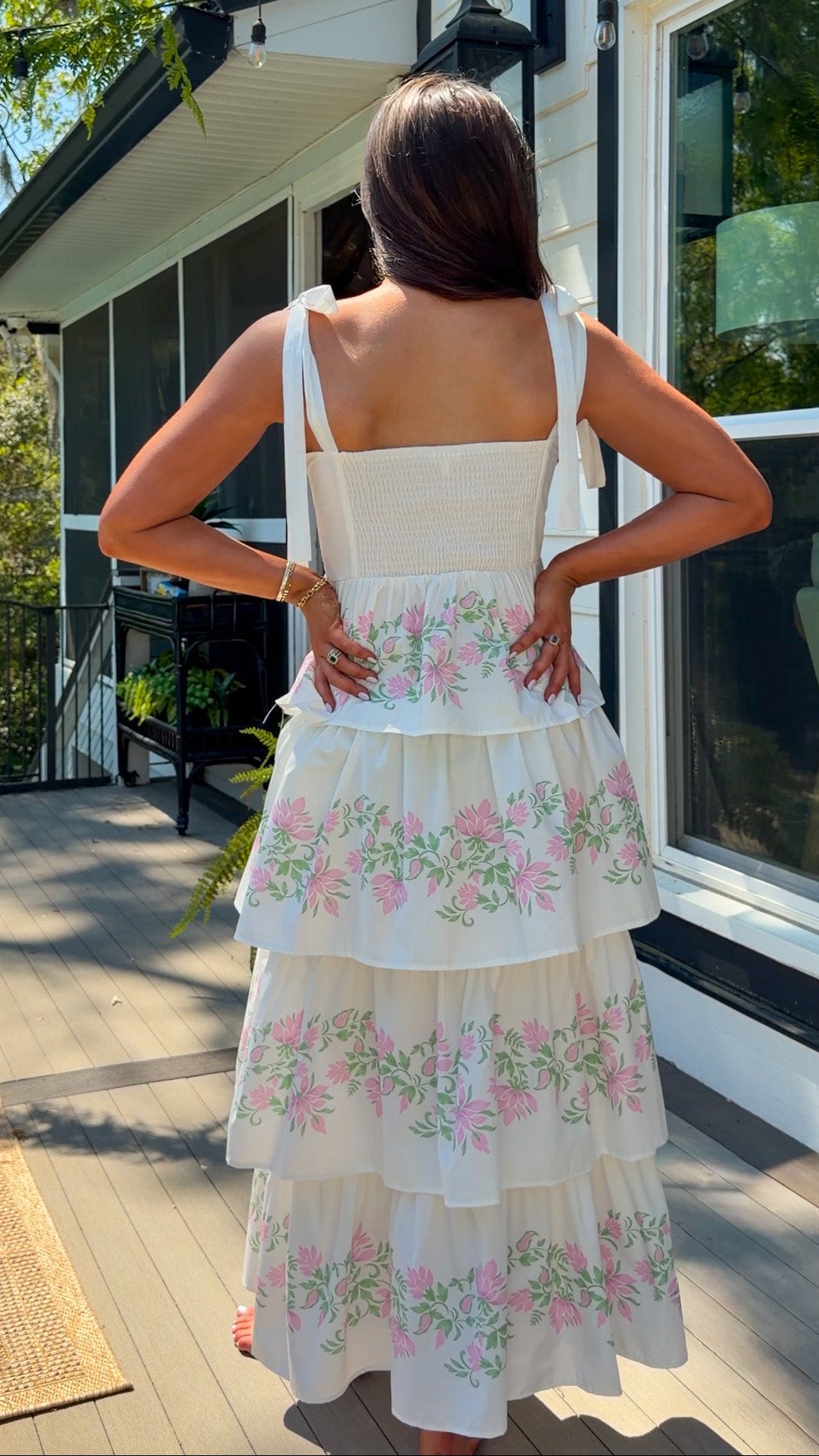 Woman in a floral dress standing on a porch with a house in the background