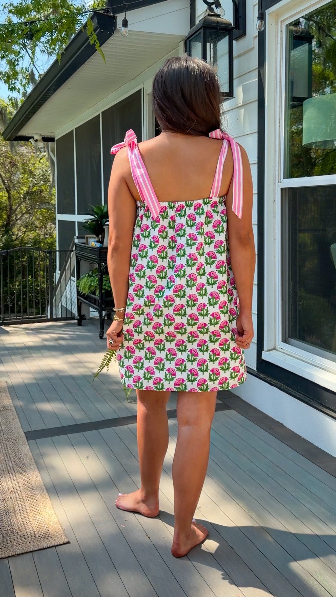 Person wearing a patterned dress standing on a wooden deck.