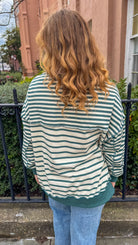 Person wearing a green and white striped shirt standing outdoors with a building and trees in the background.