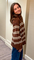 Woman wearing a brown and white striped sweater in a hallway.