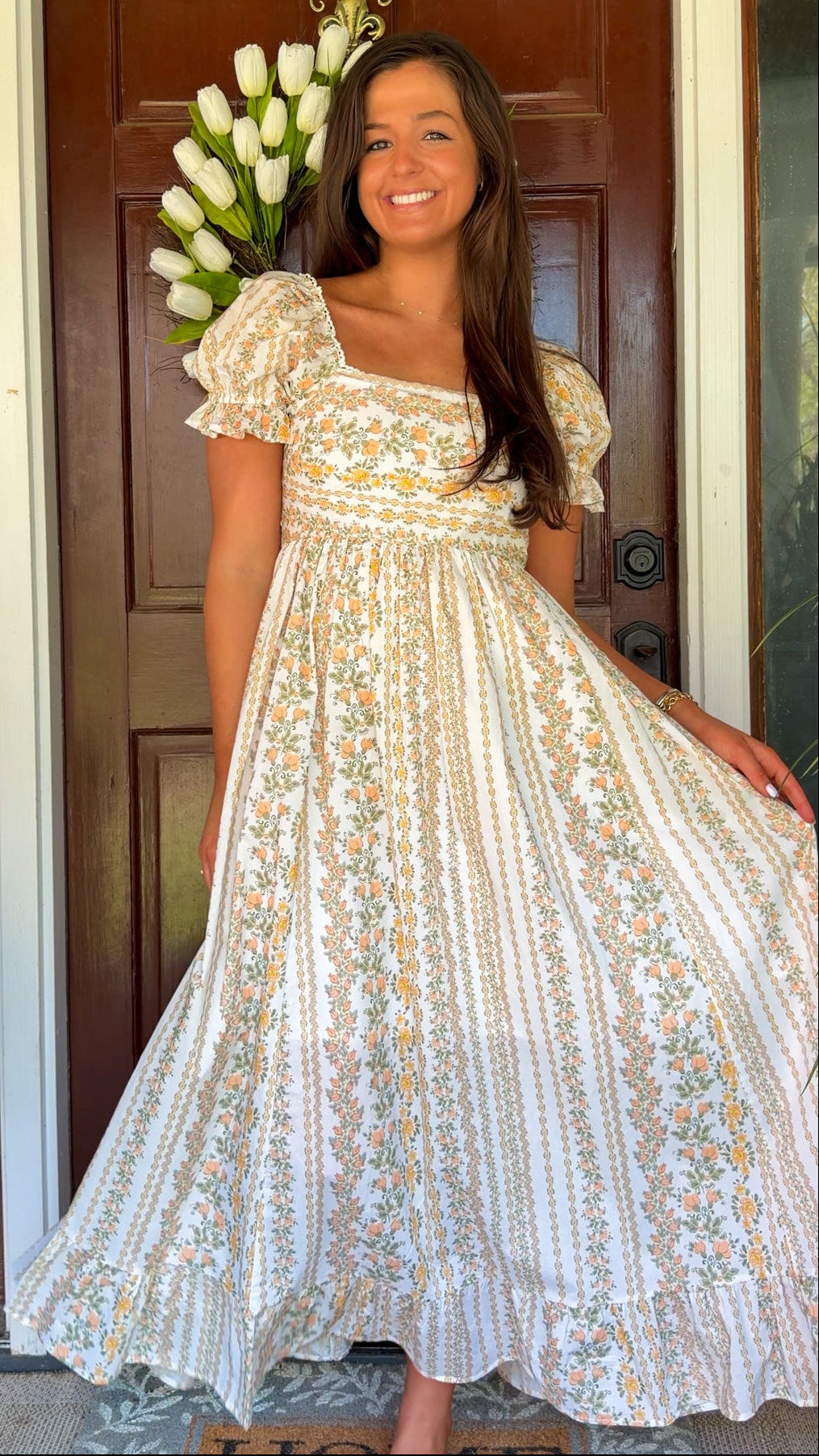 Woman in a floral dress standing in front of a door with white flowers.