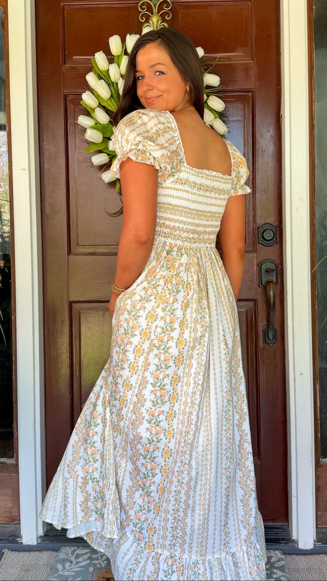 Woman in a floral dress standing in front of a door with flowers.