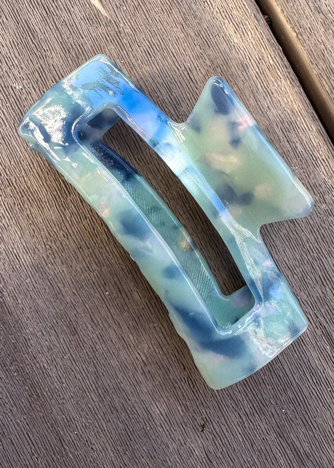 Decorative hair clip with blue and green gradient on a wooden surface