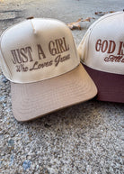 Two baseball caps with embroidered text on a concrete surface