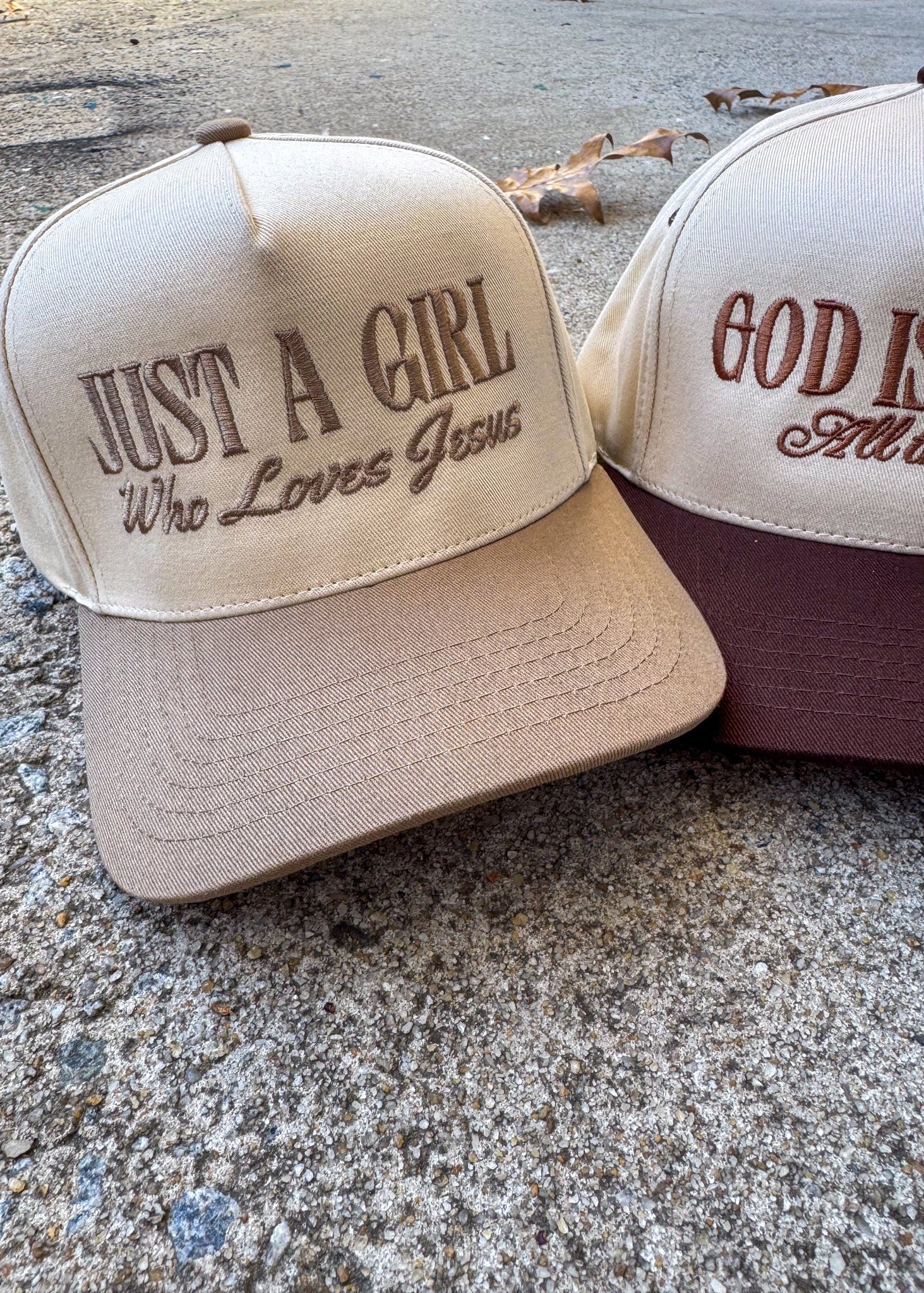 Two baseball caps with embroidered text on a concrete surface