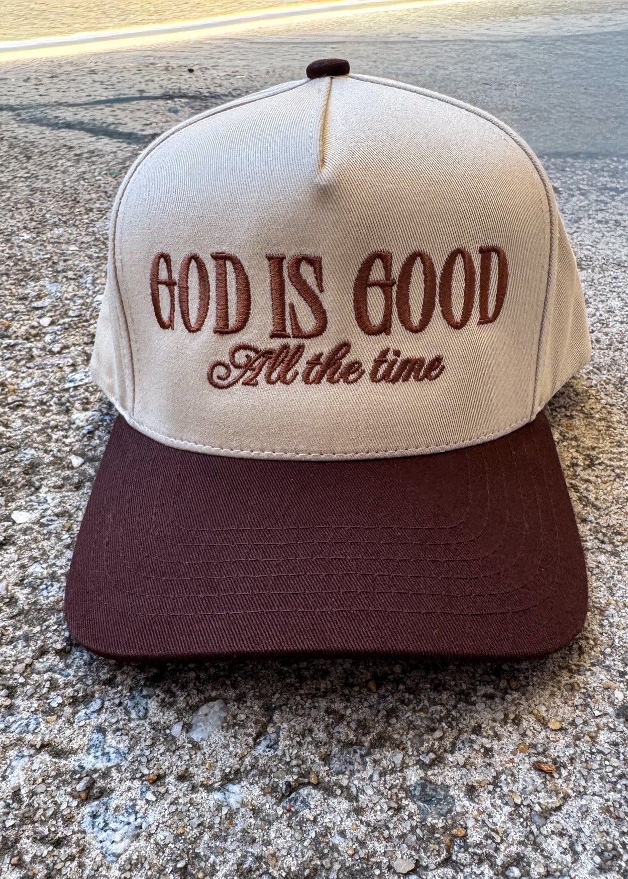 Cap with 'God is Good All the time' text on a concrete surface, trucker hat, christian trucker hat brown