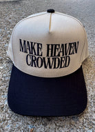 Beige and black cap with 'MAKE HEAVEN CROWDED' text on a concrete surface