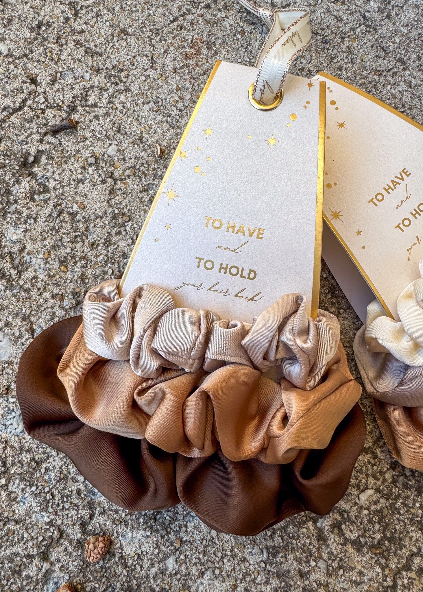 Set of three brown scrunchies with a decorative tag on a textured surface