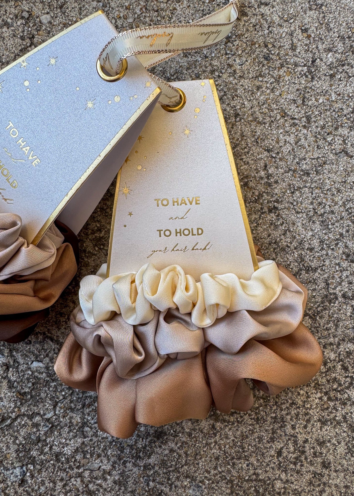 Set of beige scrunchies with a decorative tag on a textured surface
