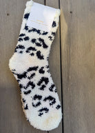 White fuzzy sock with black leopard print pattern on a wooden surface