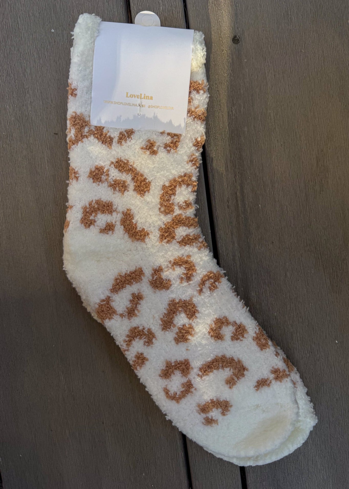 Fluffy white sock with brown leopard print pattern on a wooden surface