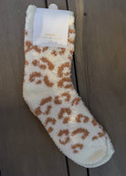 Fluffy white sock with brown leopard print pattern on a wooden surface