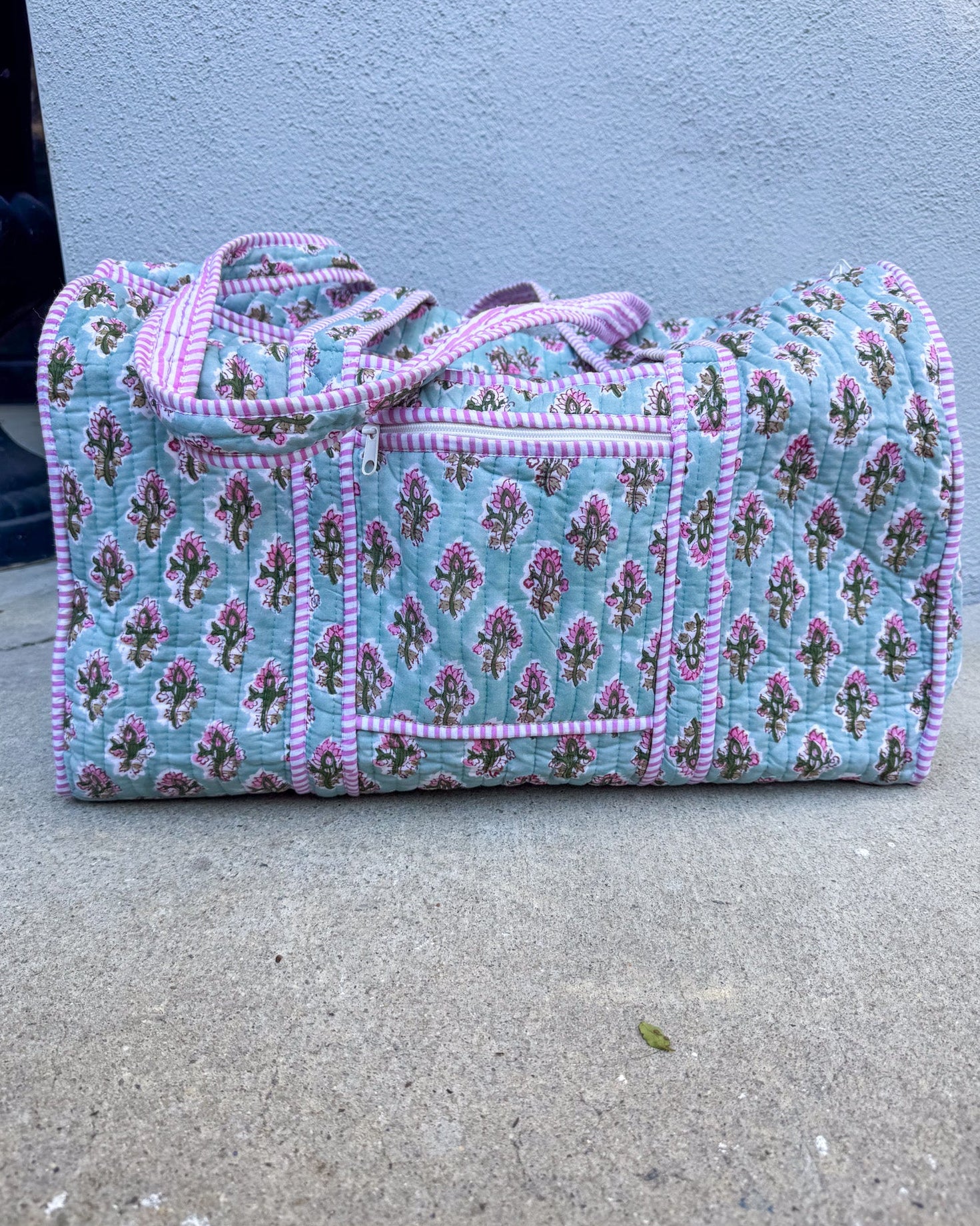 Floral patterned duffel bag with pink trim on a concrete surface.