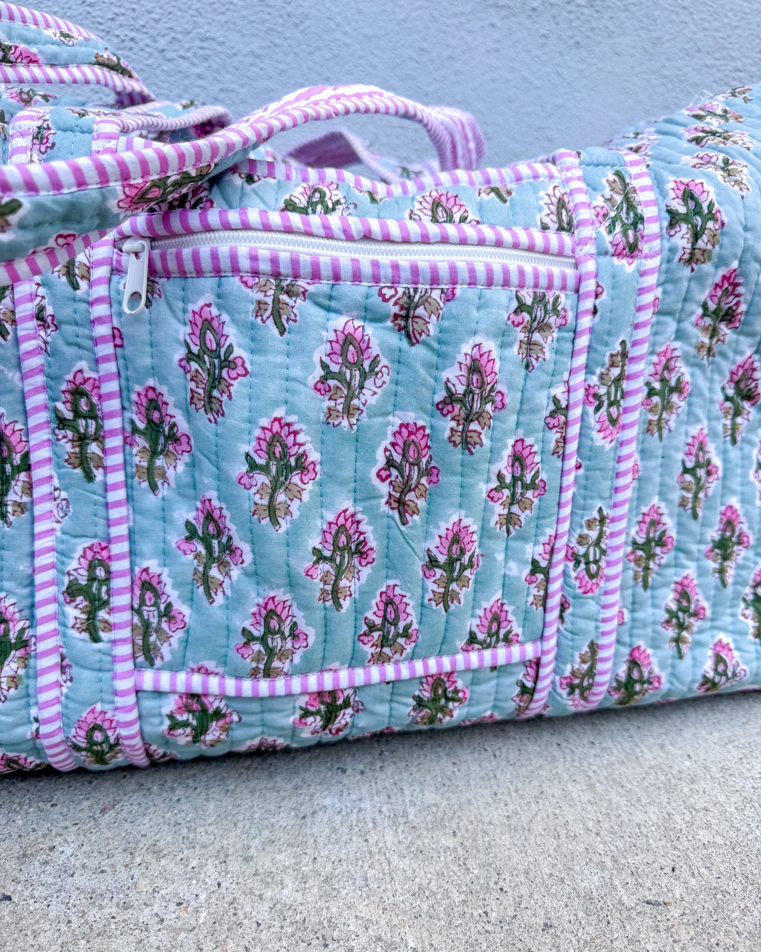 Floral quilt with pink and white striped trim on a concrete surface